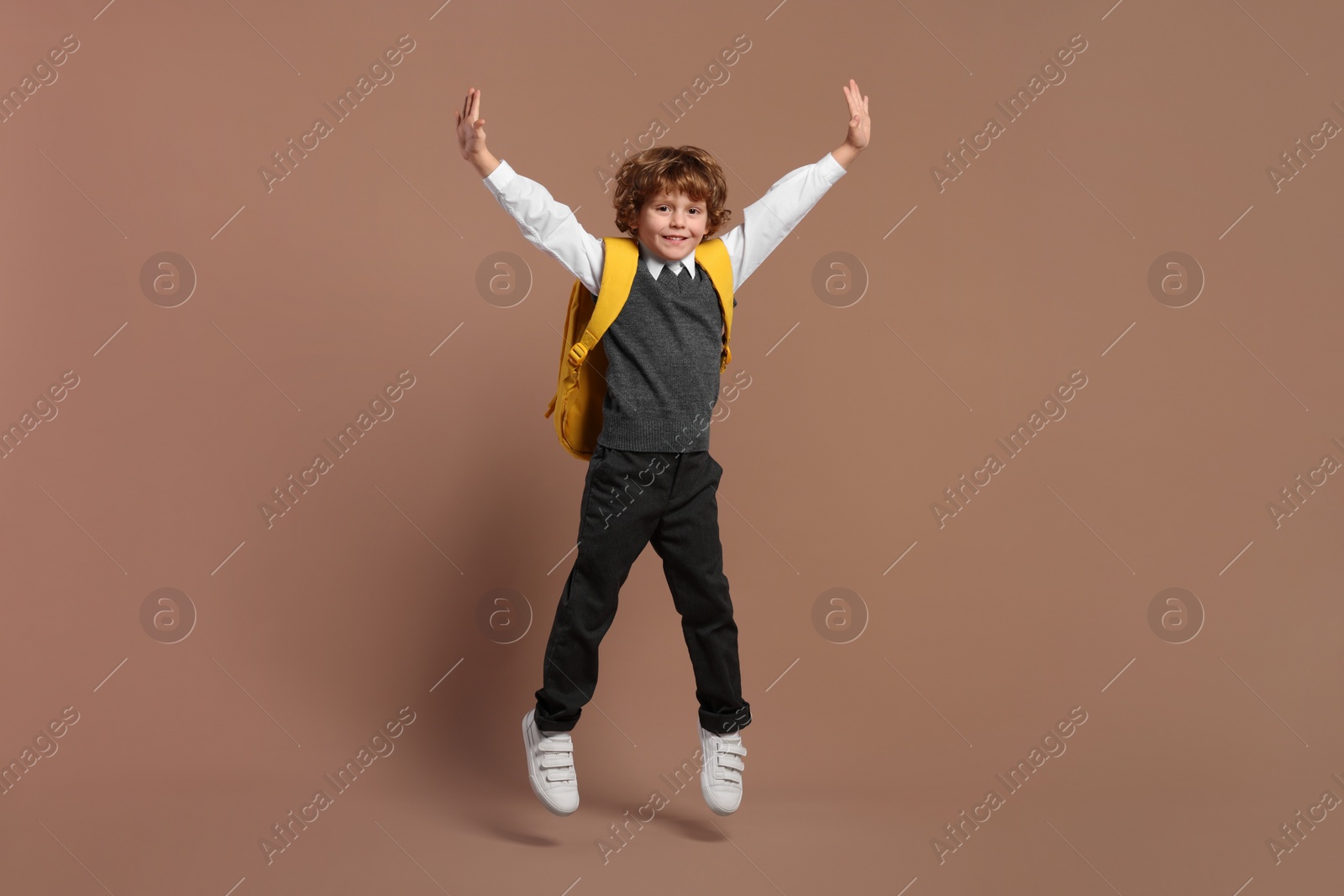 Photo of Happy schoolboy with backpack jumping on brown background