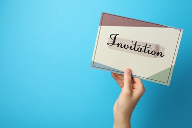 Photo of Woman holding beautiful card with word Invitation on light blue background, closeup. Space for text