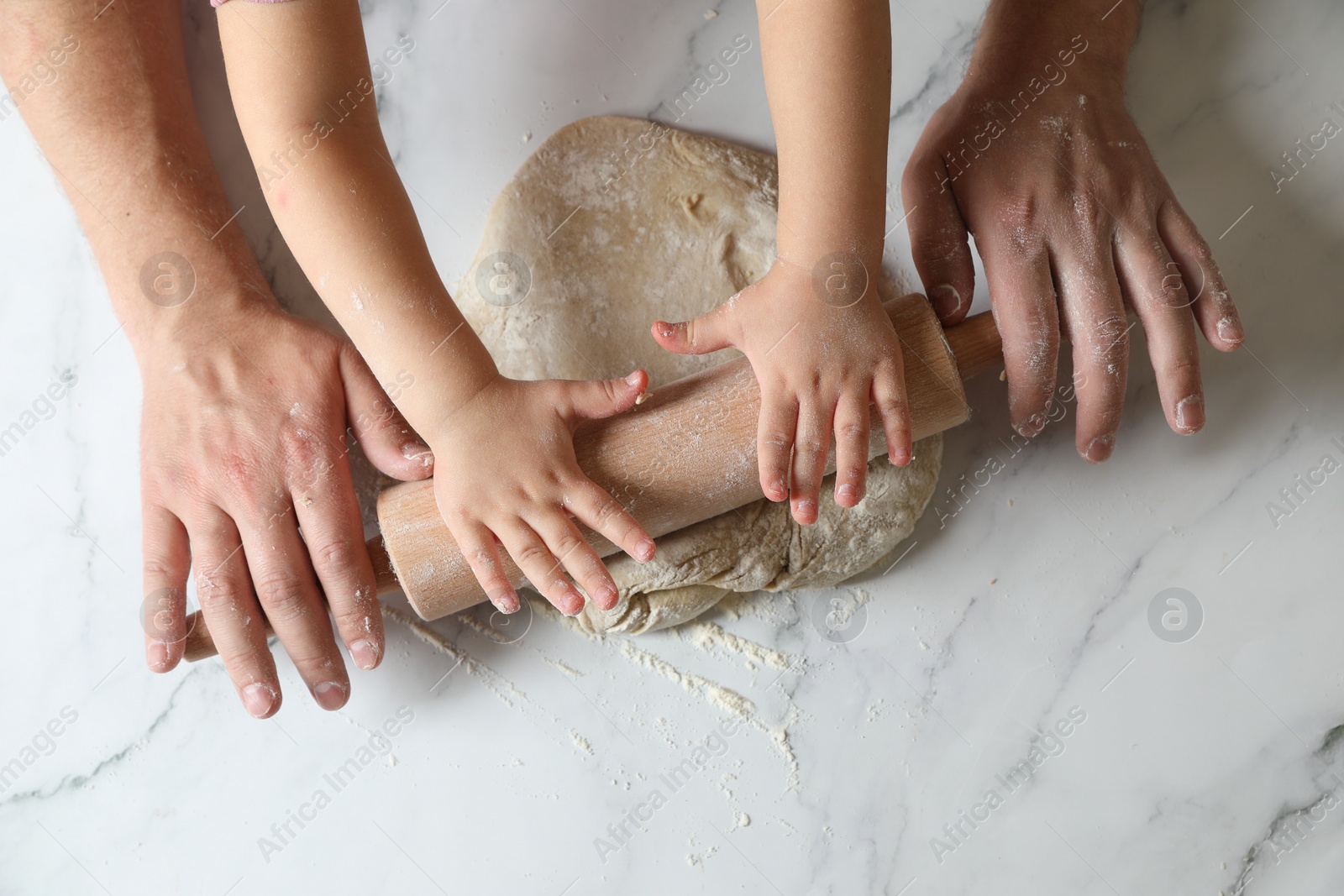 Photo of Father and child rolling raw dough at white table, top view