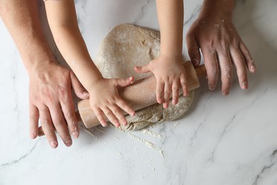 Photo of Father and child rolling raw dough at white table, top view