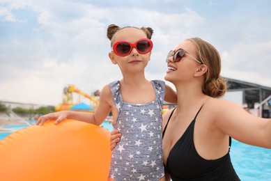 Photo of Mother and daughter with inflatable ring near pool in water park. Family vacation