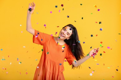 Photo of Happy woman and falling confetti on yellow background