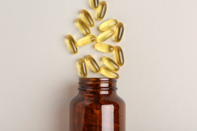 Bottle and vitamin capsules on light grey background, top view