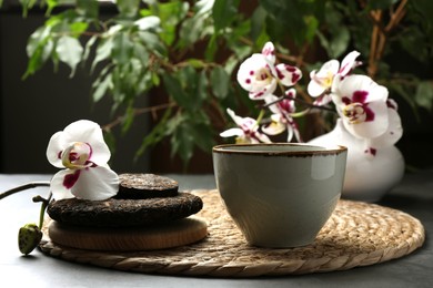 Photo of Aromatic pu-erh tea, cup and beautiful orchid on grey table, closeup