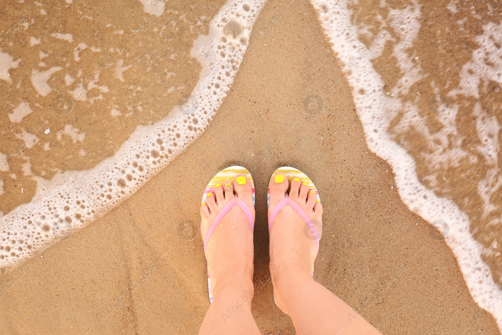 Photo of Top view of woman with stylish flip flops on sand near sea, space for text. Beach accessories