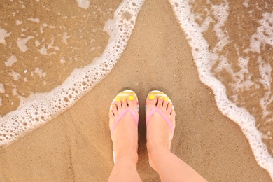 Photo of Top view of woman with stylish flip flops on sand near sea, space for text. Beach accessories