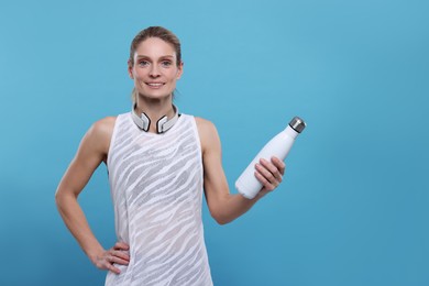 Photo of Sportswoman with thermo bottle and headphones on light blue background, space for text