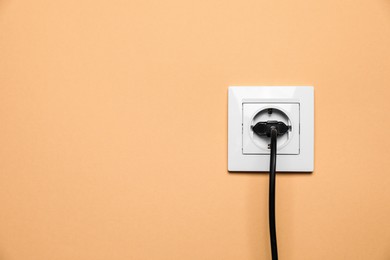 Photo of Power socket with inserted plug on pale orange wall, space for text. Electrical supply