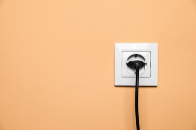 Power socket with inserted plug on pale orange wall, space for text. Electrical supply