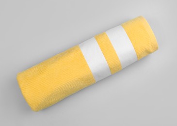 Rolled yellow beach towel on light grey background, top view