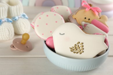 Photo of Cute tasty cookies of different shapes, pacifier and booties on white wooden table, closeup. Baby shower party