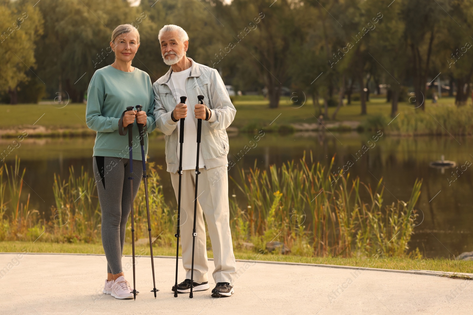 Photo of Senior man and woman with Nordic walking poles outdoors, space for text