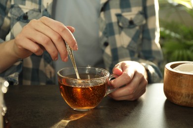 Photo of Woman stirring tea with spoon at dark table, closeup