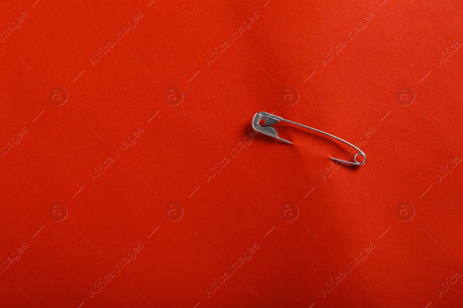 Photo of Safety pin attached on red paper, top view. Space for text