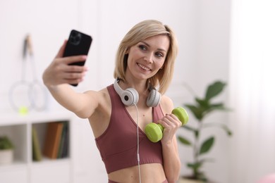 Smiling sports blogger holding dumbbell while streaming online fitness lesson with smartphone at home