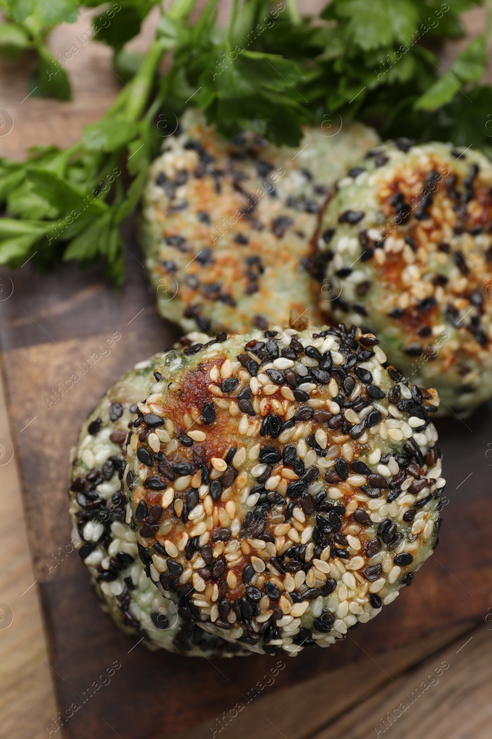 Photo of Delicious vegan cutlets with sesame and fresh parsley on wooden table, closeup