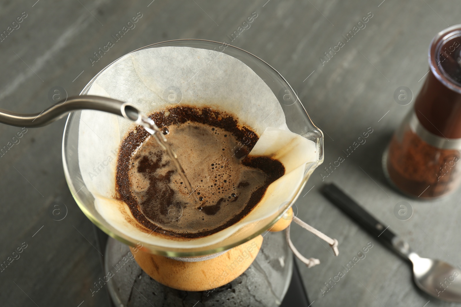 Photo of Pouring hot water into glass chemex coffeemaker with paper filter and coffee on gray table, above view