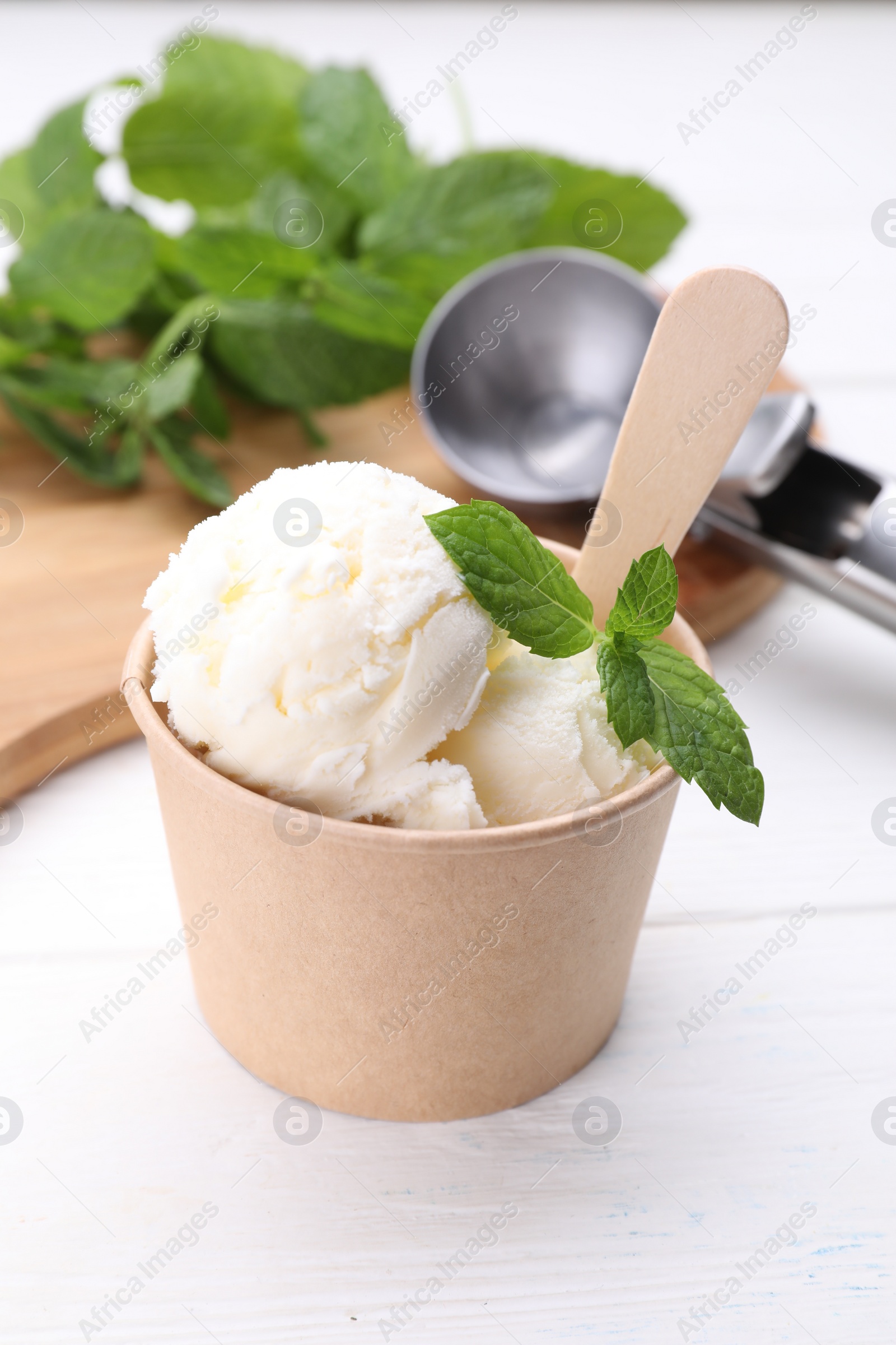 Photo of Delicious vanilla ice cream and mint in paper cup on white wooden table