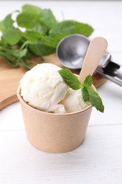 Photo of Delicious vanilla ice cream and mint in paper cup on white wooden table