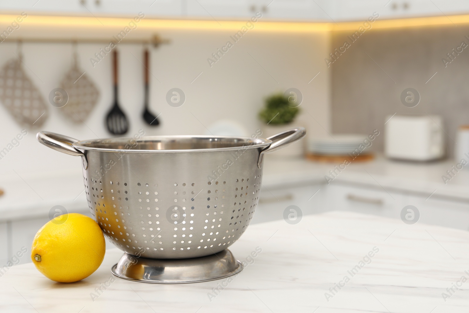 Photo of Empty colander and fresh lemon on white marble table in kitchen. Space for text