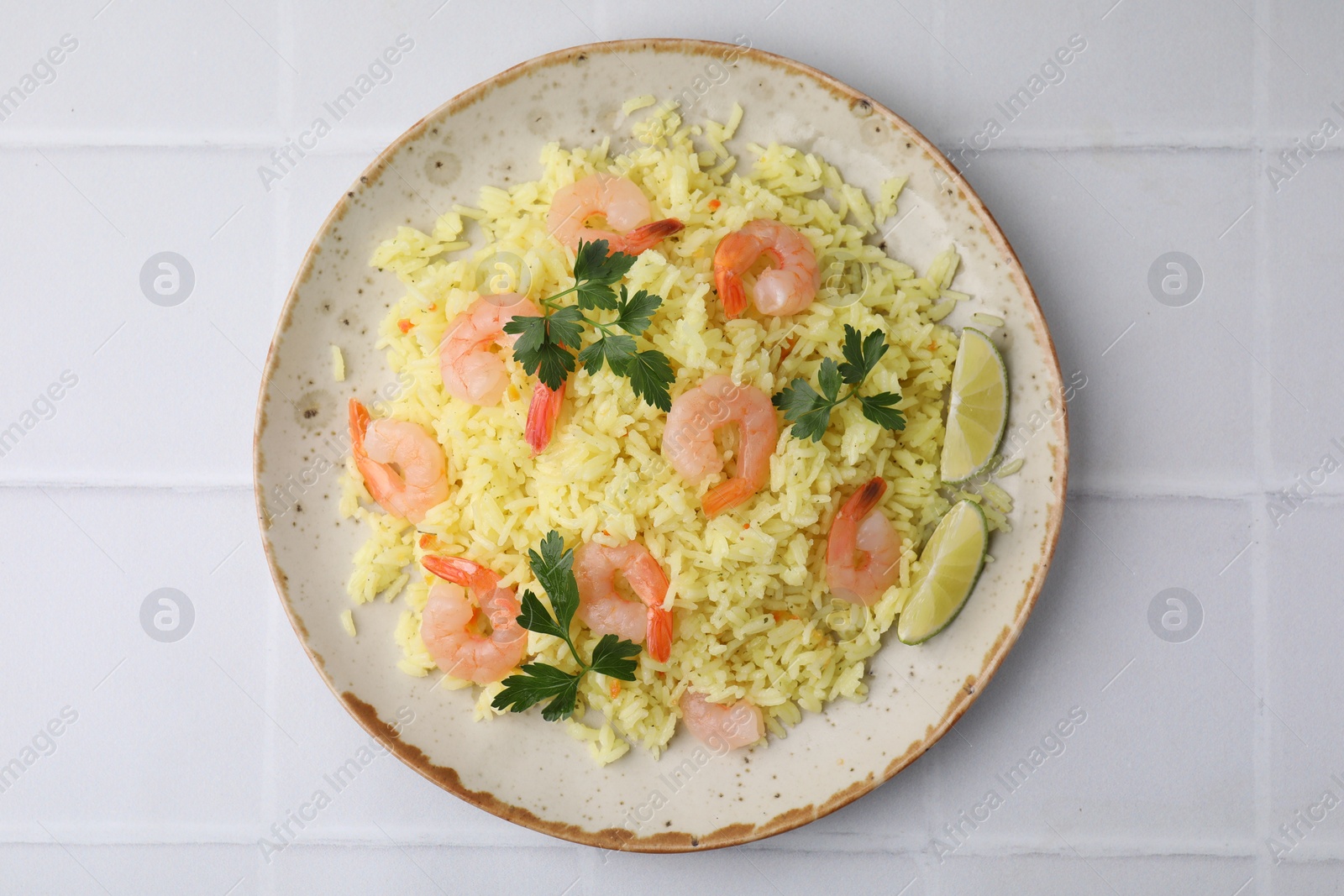 Photo of Delicious risotto with shrimps, lime and parsley on white tiled table, top view