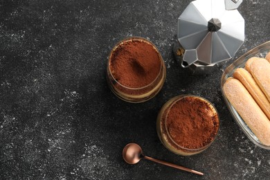 Photo of Delicious tiramisu in glasses and ingredients on grey textured table, flat lay. Space for text