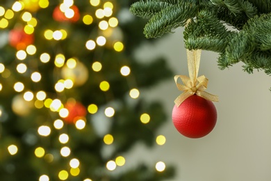 Photo of Beautiful Christmas ball hanging on fir tree branch against blurred lights, closeup. Space for text