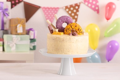 Delicious cake decorated with sweets on white wooden table in festive room