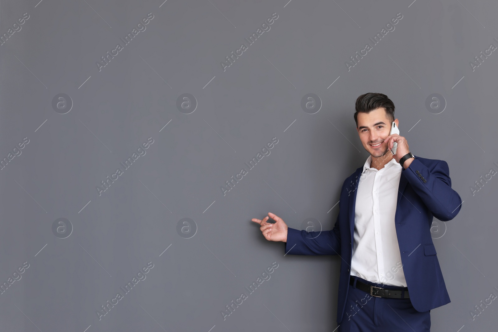 Photo of Handsome young man talking on phone against grey background. Space for text