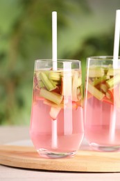 Photo of Glasses of tasty rhubarb cocktail on wooden table outdoors