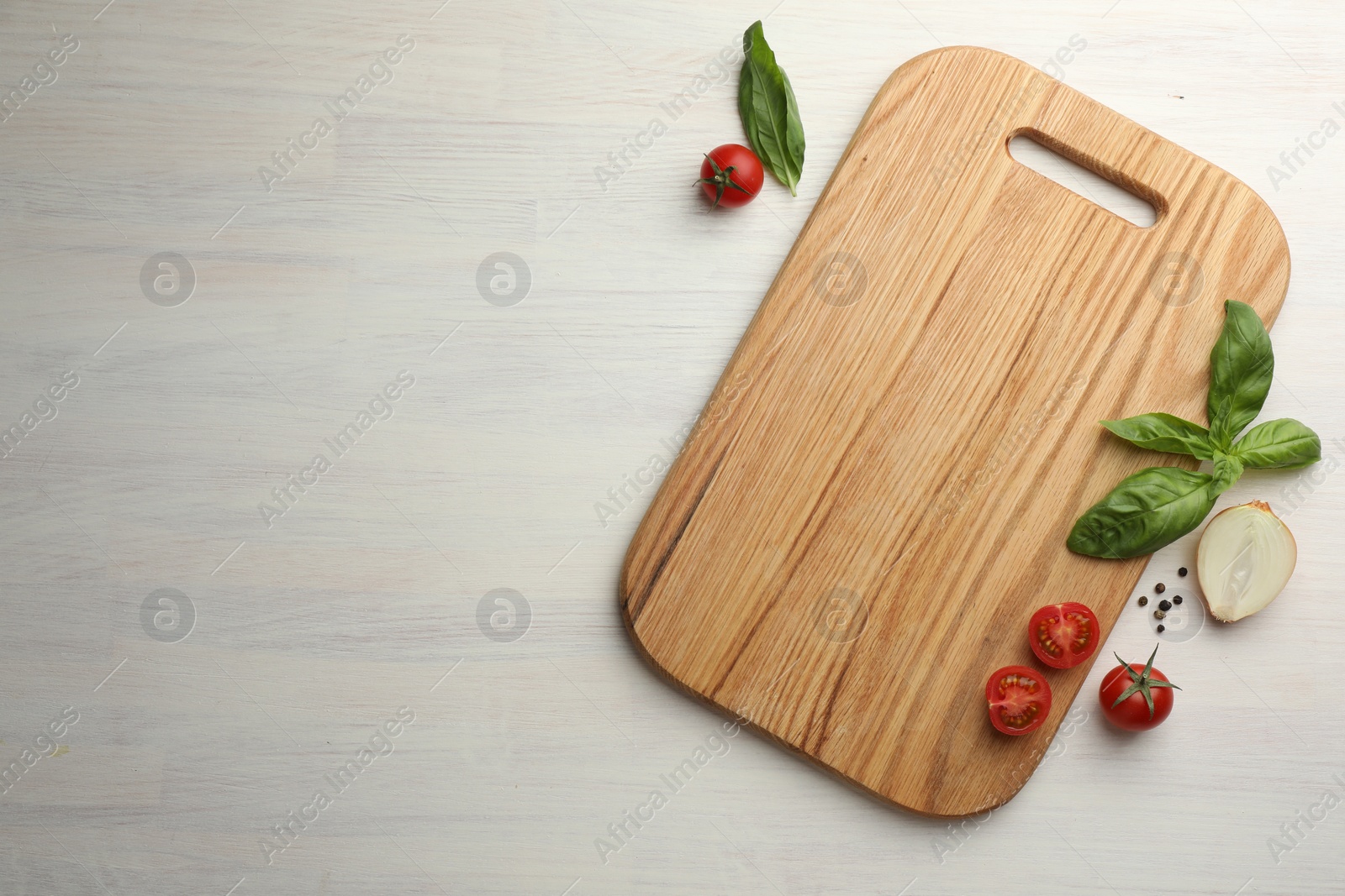 Photo of Cutting board, basil, onion, pepper and tomatoes on white wooden table, flat lay. Space for text