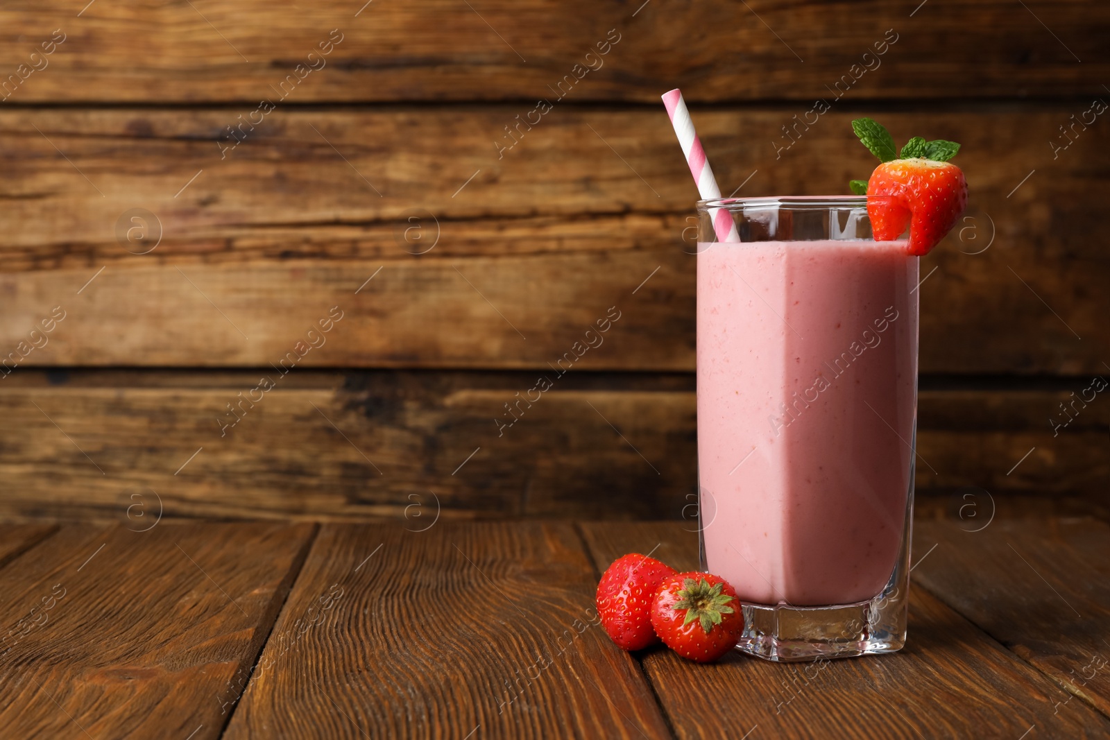 Photo of Glass with delicious berry smoothie and fresh strawberries on wooden table. Space for text