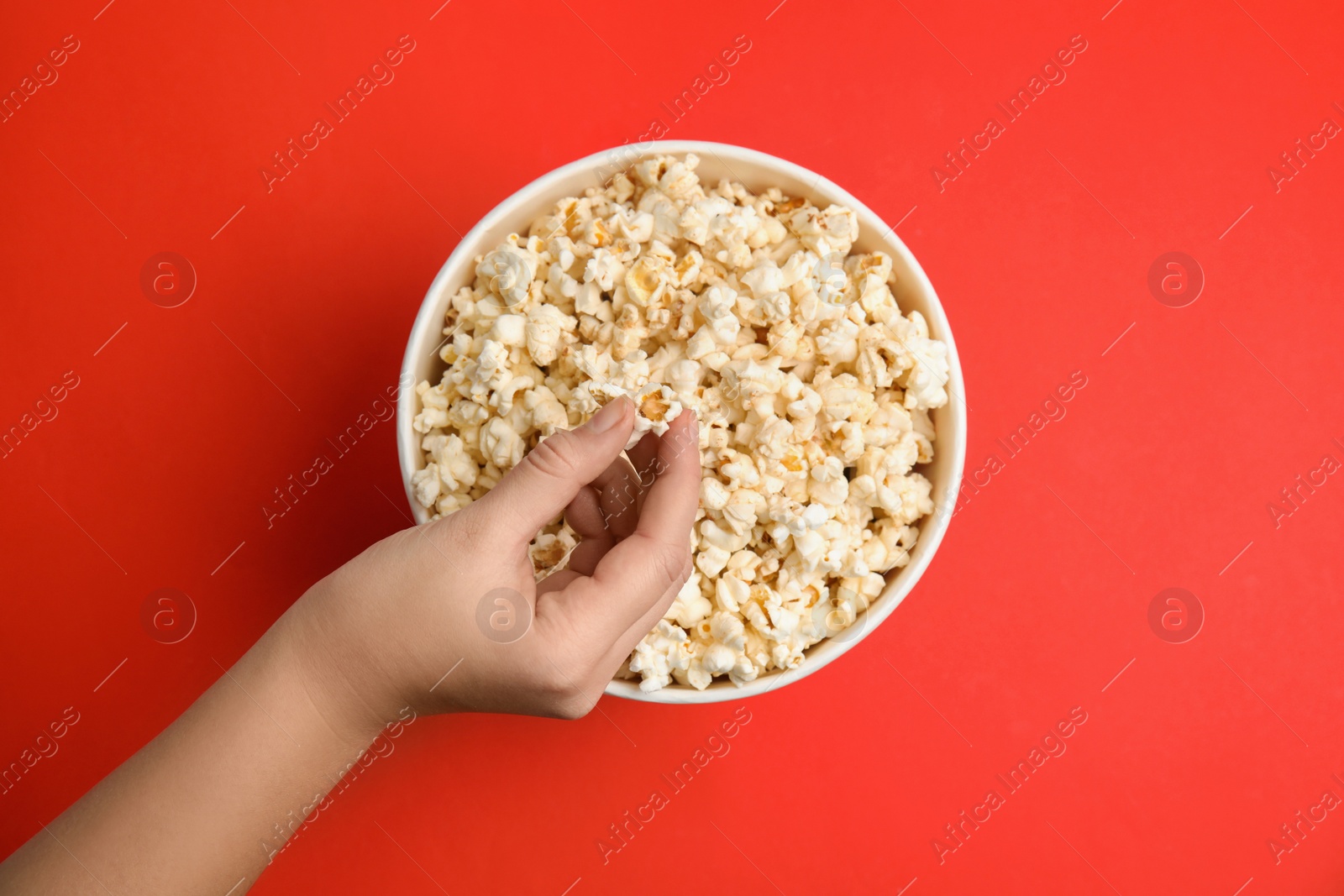 Photo of Woman taking fresh pop corn from bucket on red background, top view
