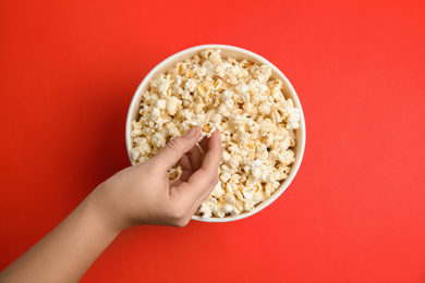 Woman taking fresh pop corn from bucket on red background, top view