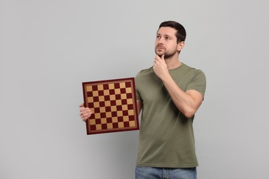 Photo of Thoughtful man holding chessboard on light grey background. Space for text