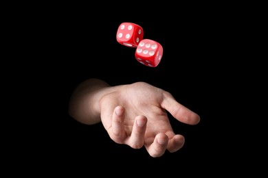 Man throwing red dice on black background, closeup