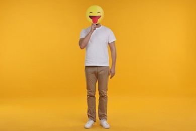 Photo of Man covering face with emoticon sticking out tongue on yellow background