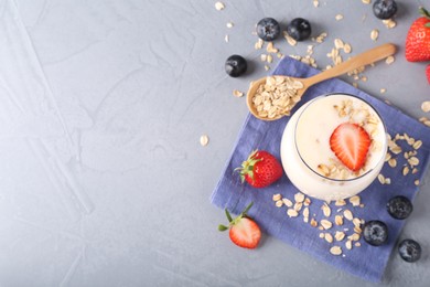 Tasty yogurt in glass, oats and berries on grey table, flat lay. Space for text