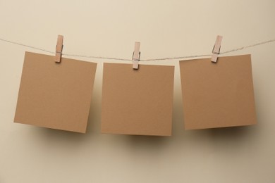 Photo of Wooden clothespins with blank notepapers on twine against beige background. Space for text