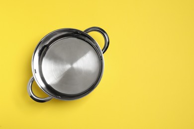 Empty steel pot on yellow background, top view. Space for text