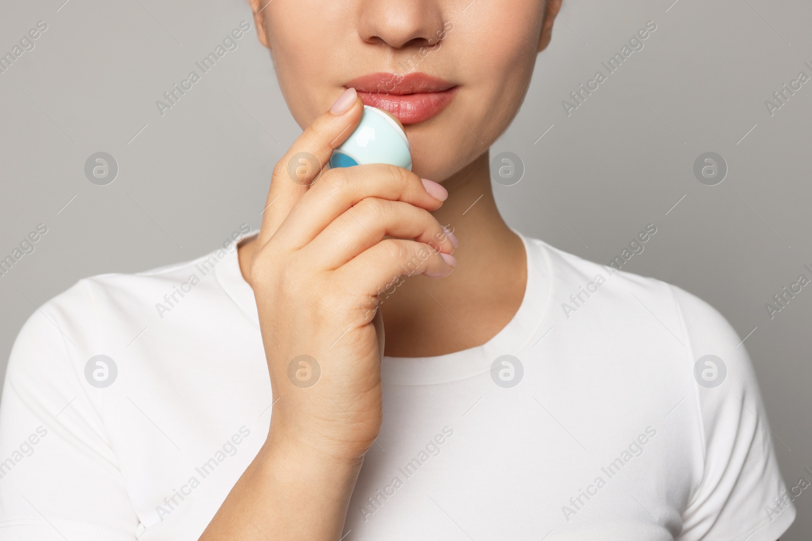 Photo of Young woman applying lip balm on grey background, closeup