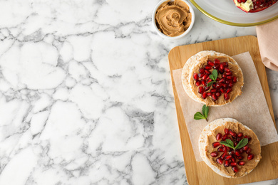 Puffed rice cakes with peanut butter and pomegranate seeds on white marble table, flat lay. Space for text