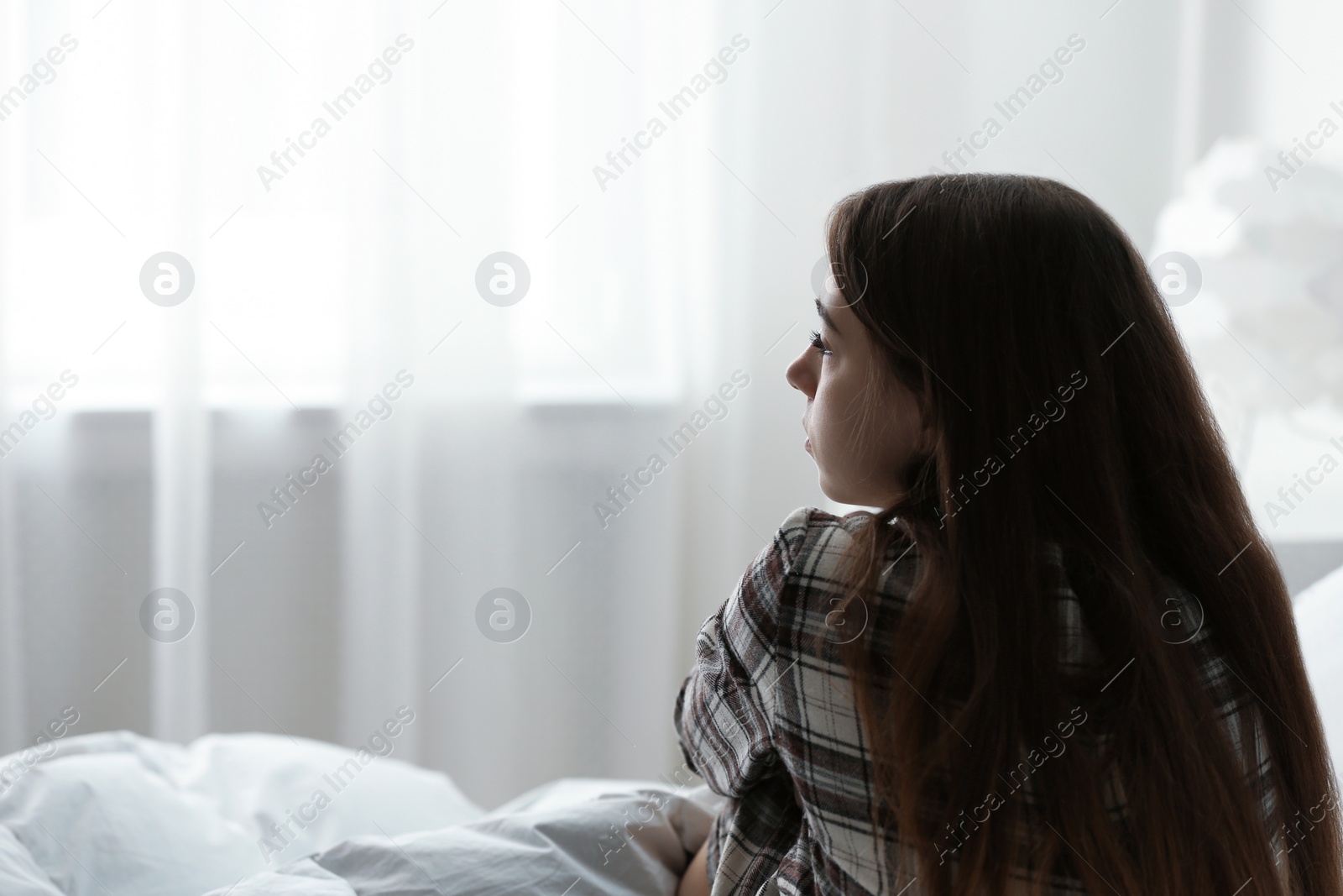 Photo of Upset teenage girl sitting on bed. Space for text