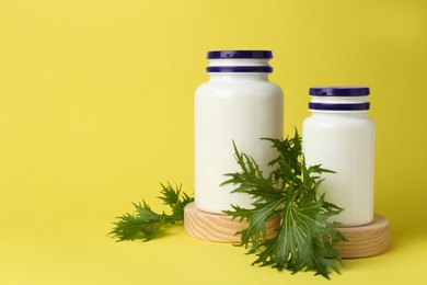 Photo of Medicine bottles and green leaf on yellow background, space for text