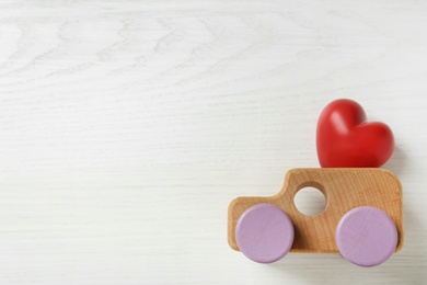 Photo of Red heart and wooden toy car on white background, flat lay with space for text. Happy Valentine's Day