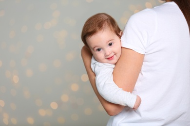 Young mother holding cute baby against  defocused lights. Space for text