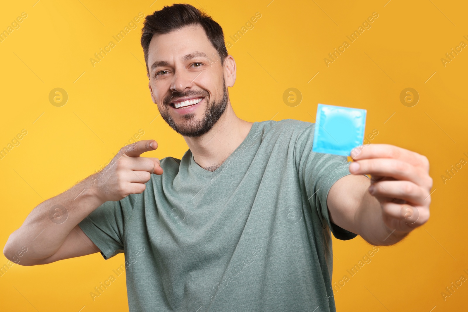 Photo of Happy man holding condom on orange background