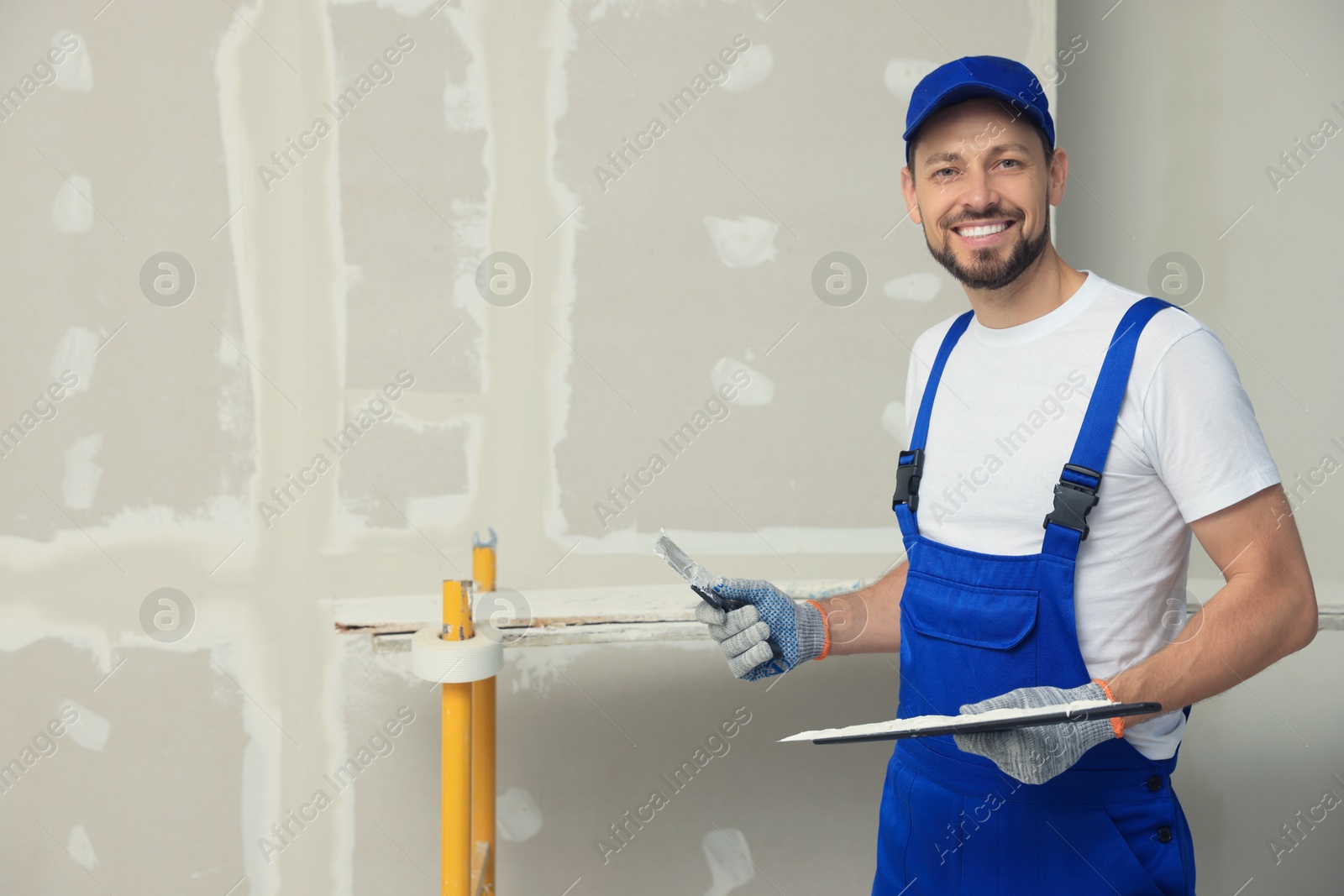 Photo of Professional worker with putty knives near wall. Space for text