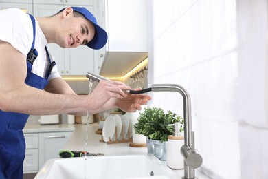 Photo of Smiling plumber examining metal faucet in kitchen