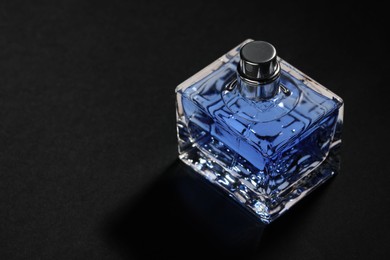 Photo of Blue men's perfume in bottle on black background, space for text